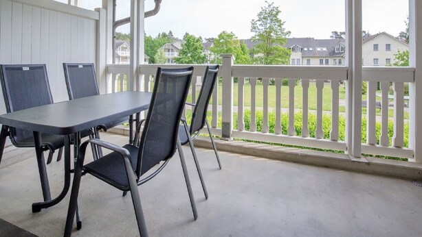 A covered outdoor area with a table and chairs, a white railing, and a view of houses in the background.