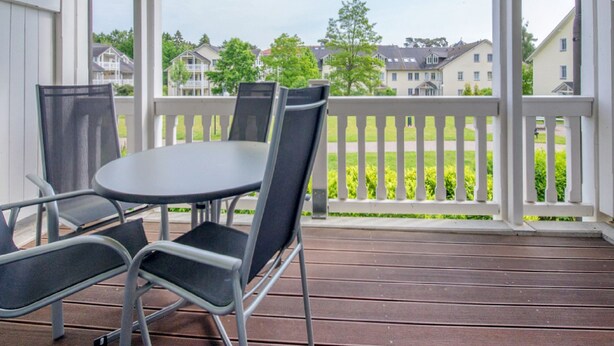 A covered outdoor area with a table and chairs, a white fence, and houses in the background.