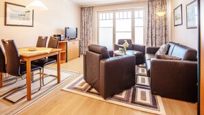 A modern living room with a dining area, a sofa set, a television, and a large window with curtains.