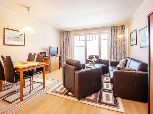 A modern living room with a dining area, a sofa set, a television, and a large window with curtains.