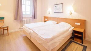 A hotel room with a double bed, a wooden nightstand, a chair, a window with curtains, and a framed picture on the wall.