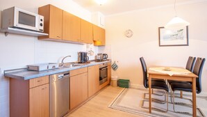 A compact kitchen with modern appliances, a dining area with a table and chairs, and a small trash bin.