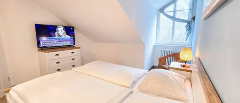 A bedroom with a TV on a dresser, a window with curtains, and a lamp on a nightstand.