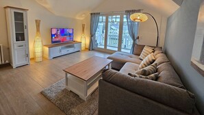 Ein modernes Wohnzimmer mit Fernseher, Sofa, Couchtisch und dekorativen Lampen.