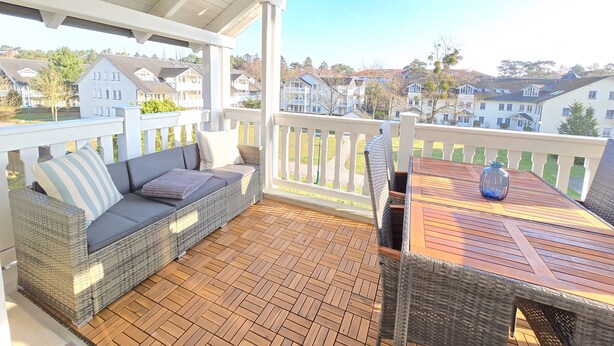 Ein überdachter Außenbereich mit Rattan-Sofa und Holztisch, mit Blick auf eine Wohngegend.
