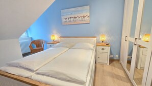 Ein Schlafzimmer mit einem großen Bett, zwei Nachttischen mit Lampen, einem Korbstuhl und einem Vogelgemälde an der Wand.