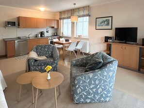 A compact living space with a kitchenette, two sofas, a dining table, and a TV.