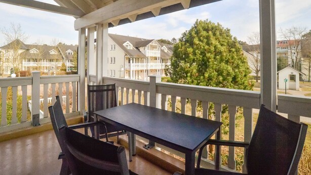 A covered outdoor area with a table and chairs, overlooking a residential neighborhood with houses and a large evergreen tree. - Comfort apartment with 1 bedroom and balcony on the upper floor (Ostseebad Binz)