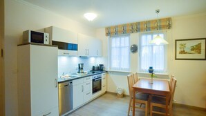 A compact kitchen with white cabinets, a microwave, a coffee maker, and a dining table with chairs. - Comfort apartment with 1 bedroom and balcony on the upper floor (Ostseebad Binz)