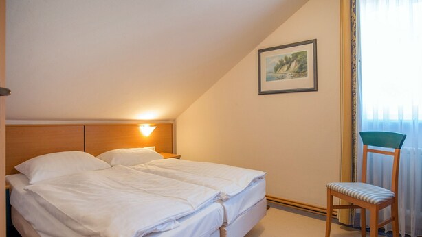 A bedroom with a bed, a nightstand, a chair, and a painting on the wall. - Comfort apartment with 1 bedroom and balcony on the top floor (Ostseebad Binz)