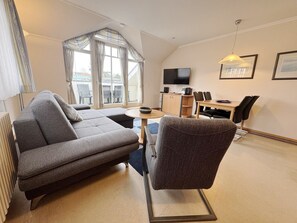 A modern living room with a sofa, a chair, a small table, a TV, and a dining area with chairs and a table.