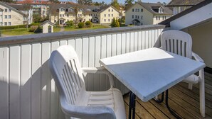 A balcony with a white table and two white chairs, overlooking a row of houses. - Comfort apartment with 1 bedroom and balcony on the top floor (Ostseebad Binz)