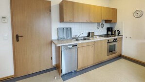 A compact kitchen with wooden cabinets, a dishwasher, a stove, and a coffee maker. - Comfort apartment with 1 bedroom and balcony on the top floor (Ostseebad Binz)