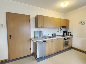 A compact kitchen with wooden cabinets, a dishwasher, a stove, and a coffee maker. - Comfort apartment with 1 bedroom and balcony on the top floor (Ostseebad Binz)