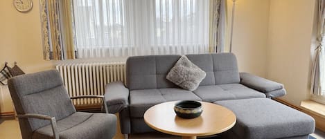 A modern living room with a grey sofa, a round wooden coffee table, and a grey armchair.