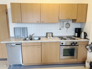 A compact kitchen with wooden cabinets, a stainless steel sink, a Siemens dishwasher, a stove with four burners, and an oven. - Comfort Apartment with 1 bedroom and a balcony on the top floor (Ostseebad Binz)