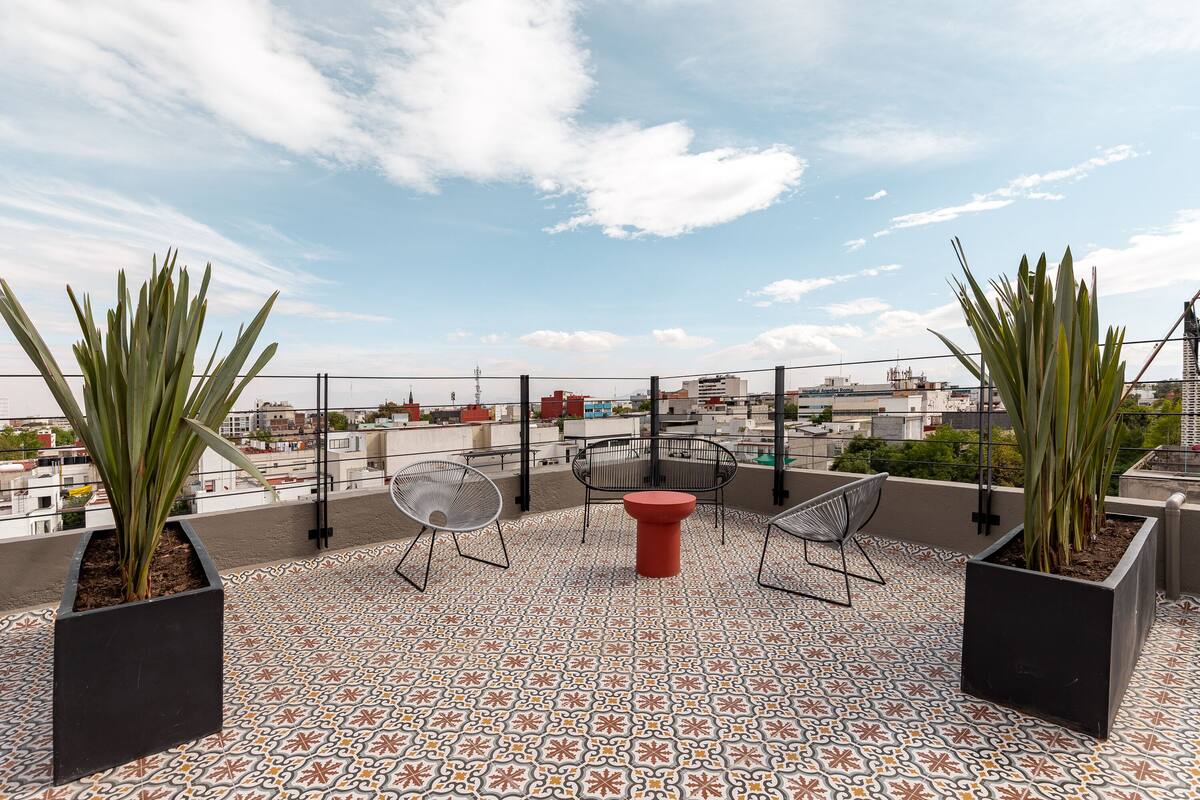Terraço no telhado com piso estampado, duas plantas em vasos e móveis de exterior.