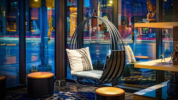 A modern interior with a hanging chair, round ottomans, and a view of a busy street at night. - Renaissance Oklahoma City Downtown Bricktown Hotel (Oklahoma City)
