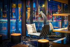 A modern interior with a hanging chair, round ottomans, and a view of a busy street at night.