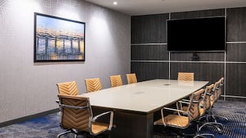 A conference room with a long table, six chairs, a large flat-screen TV, and a framed picture on the wall.