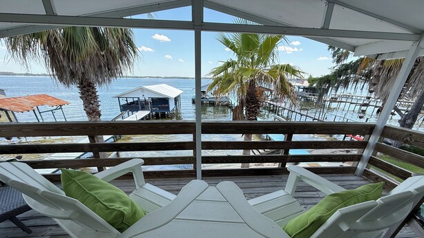 A wooden deck with white lounge chairs and a table, overlooking a marina with boats and a dock. - KINGSLEY LAKE! Spring fed, best lake in Fl, great fishing, waterskiing… (Starke)