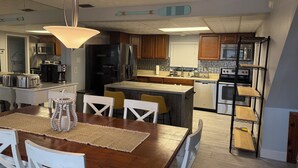 A modern kitchen with a central island, stainless steel appliances, and a dining area with a wooden table and white chairs. - KINGSLEY LAKE! Spring fed, best lake in Fl, great fishing, waterskiing… (Starke)