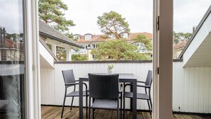 En balkon med et bord og stole, udsigt over et boligområde med træer og huse.