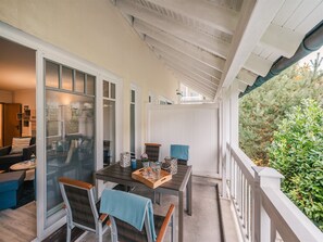 Een overdekt terras met een tafel en stoelen, een schuifpui naar een woonkamer en uitzicht op groen.