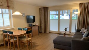 A modern living room with a wooden dining table, blue chairs, a grey sofa, and a television on a stand. - Comfort apartment with 1 bedroom and balcony on the upper floor (Ostseebad Binz)
