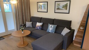 A modern living room with a grey sectional sofa, a round wooden coffee table, and two framed artworks on the wall. - Comfort apartment with 1 bedroom and balcony on the upper floor (Ostseebad Binz)