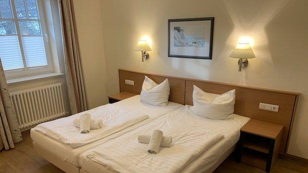A double bed with two pillows and two towels, bedside tables, a wall-mounted lamp, and a framed picture on the wall. - Comfort apartment with 1 bedroom and balcony on the upper floor (Ostseebad Binz)