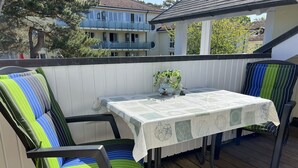 Une terrasse en bois avec une table et des chaises, un pot de fleurs et une vue sur un immeuble d’habitation.