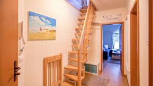 Un escalier en bois mène à un espace de vie agrémenté d’une pancarte « Bienvenue », d’un tableau accroché au mur et d’une porte sur laquelle sont fixés un téléphone et une boîte aux lettres.