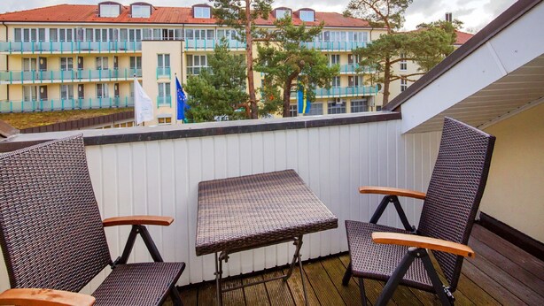 Un balcone con mobili in vimini, che si affaccia su un edificio con diversi balconi e alberi.