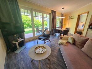 Un vaste espace de vie comprenant un canapé, une table ronde agrémentée d’un plateau décoratif, un téléviseur posé sur un meuble, ainsi qu’un coin repas avec des chaises et une table.