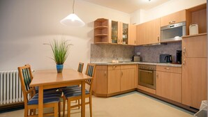A modern kitchen with wooden cabinets, a built-in oven, and a dining area with a table and chairs. - Comfort apartment with 2 bedrooms and terrace on the first floor (Ostseebad Binz)