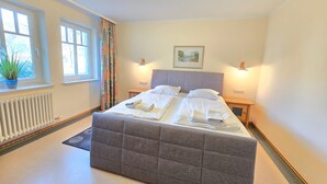 A neatly made bed with white linens and towels, a grey upholstered headboard, and two bedside tables with lamps. - Comfort apartment with 2 bedrooms and terrace on the first floor (Ostseebad Binz)