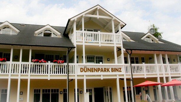A two-story building with a balcony and a sign reading "DÜNENPARK BINZ". - Comfort apartment with 2 bedrooms and terrace on the first floor (Ostseebad Binz)