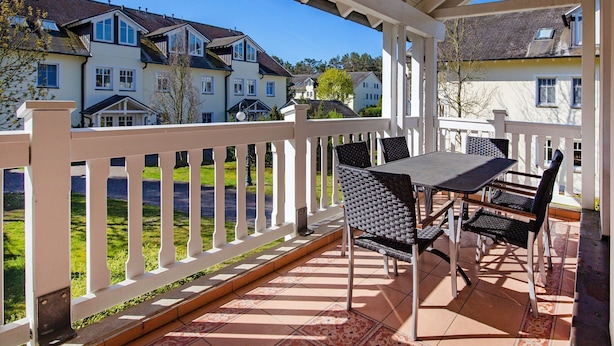 Een overdekt terras met een tafel, stoelen, een witte balustrade en uitzicht op omliggende huizen.