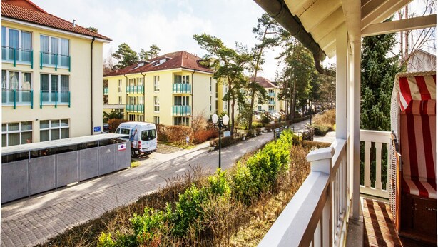 En bostadsgata med flerfamiljshus, en parkerad skåpbil och en trottoar med planteringar.