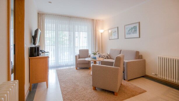 A modern living room with a sofa, armchairs, a coffee table, a TV on a stand, and a radiator. - Comfort apartment with 2 bedrooms and balcony on the upper floor (Ostseebad Binz)