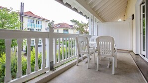 A covered patio with white chairs and a white railing, overlooking a residential area with houses and greenery. - Comfort apartment with 2 bedrooms and balcony on the upper floor (Ostseebad Binz)