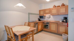 A compact kitchen with wooden cabinets, a microwave, an oven, and a dining table with chairs. - Comfort apartment with 2 bedrooms and balcony on the upper floor (Ostseebad Binz)