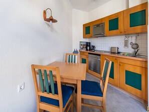 A compact kitchen with wooden cabinets, a built-in oven, and a dining area with two chairs and a table. - Comfort apartment with 1 bedroom and balcony on the top floor (Ostseebad Binz)