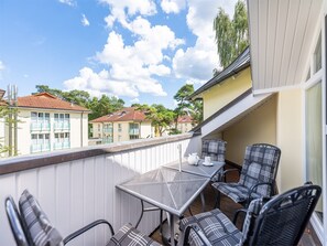 A balcony with a table and chairs, overlooking a residential area with houses and trees.
