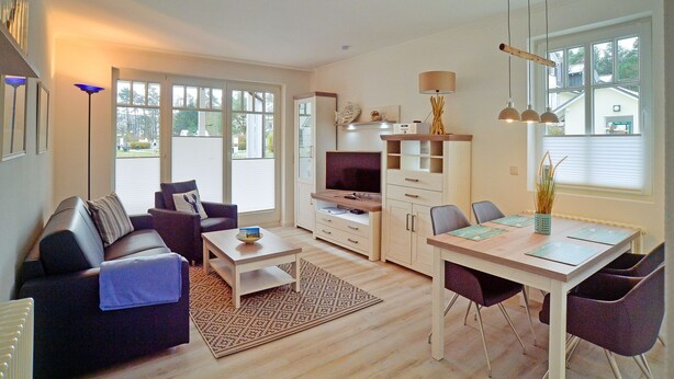Een moderne woonkamer met een bank, salontafel, televisie en een eethoek met stoelen en een tafel.