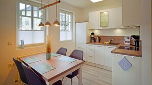 Een moderne keuken met witte kasten, een houten aanrechtblad en een ingebouwde oven. Drie hanglampen hangen boven de eettafel, waarop een placemat en een vaas met potloden staan.