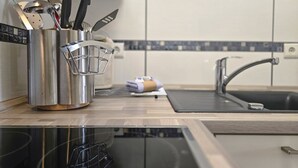 Moderni keittiö, jossa on ruostumattomasta teräksestä valmistetut kodinkoneet, pesuallas ja astiateline työtasolla.