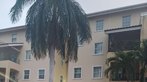 A multi-story residential building with a white picket fence, a palm tree, and a parked car. -  Enchanted at winchester kick back and relax at this modern stylish apartment  
 (Kingston)