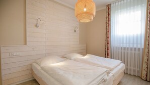 Een slaapkamer met een houten hoofdbord, een bed met wit beddengoed, een hanglamp en een raam met dunne gordijnen.